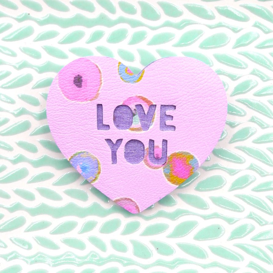 A romantic gift for a loved one. A handmade heart brooch in pastel pink polka dot unique fabric and wood with the phrase Love You cut from it