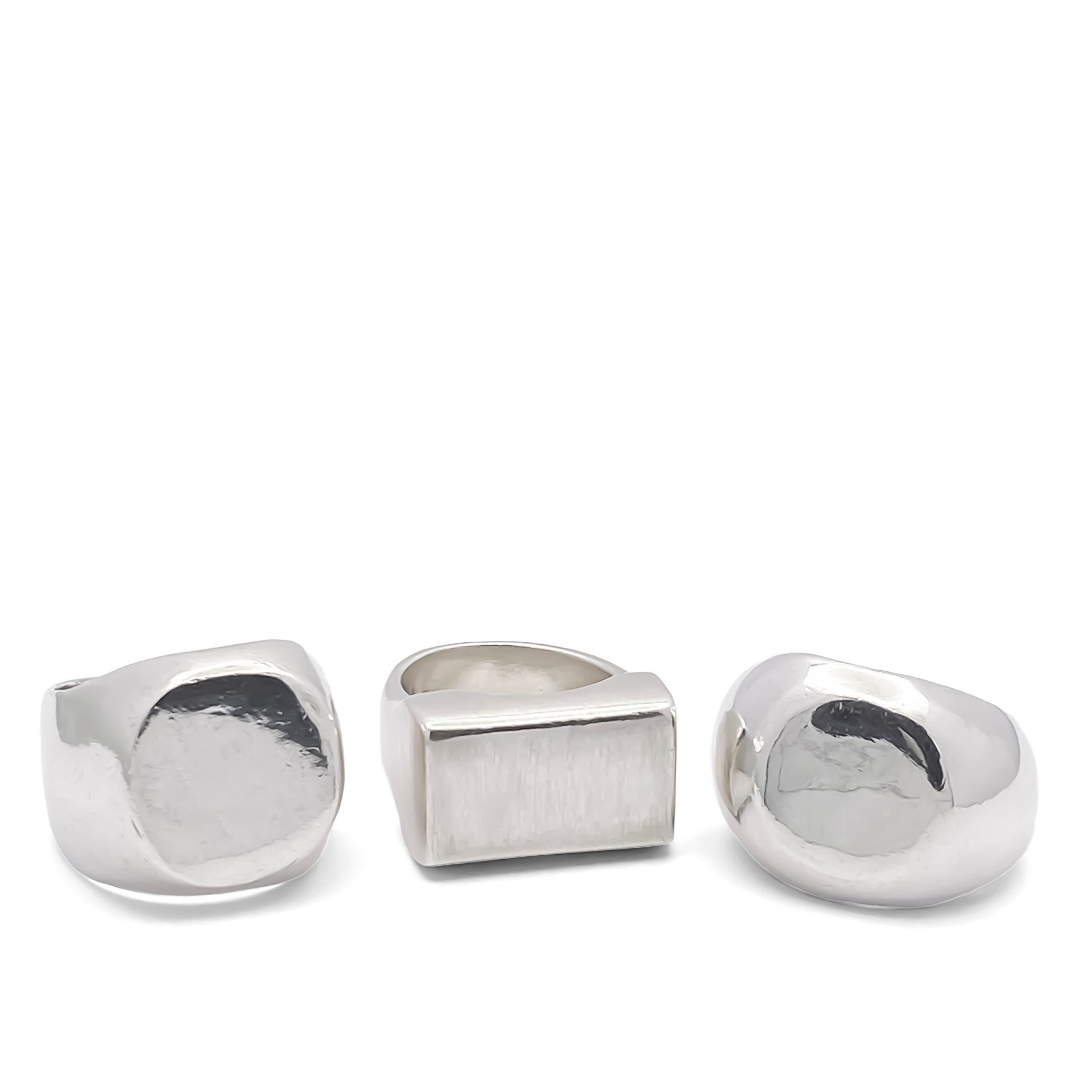 Three handcrafted silver signet rings with different face shapes displayed on a white background