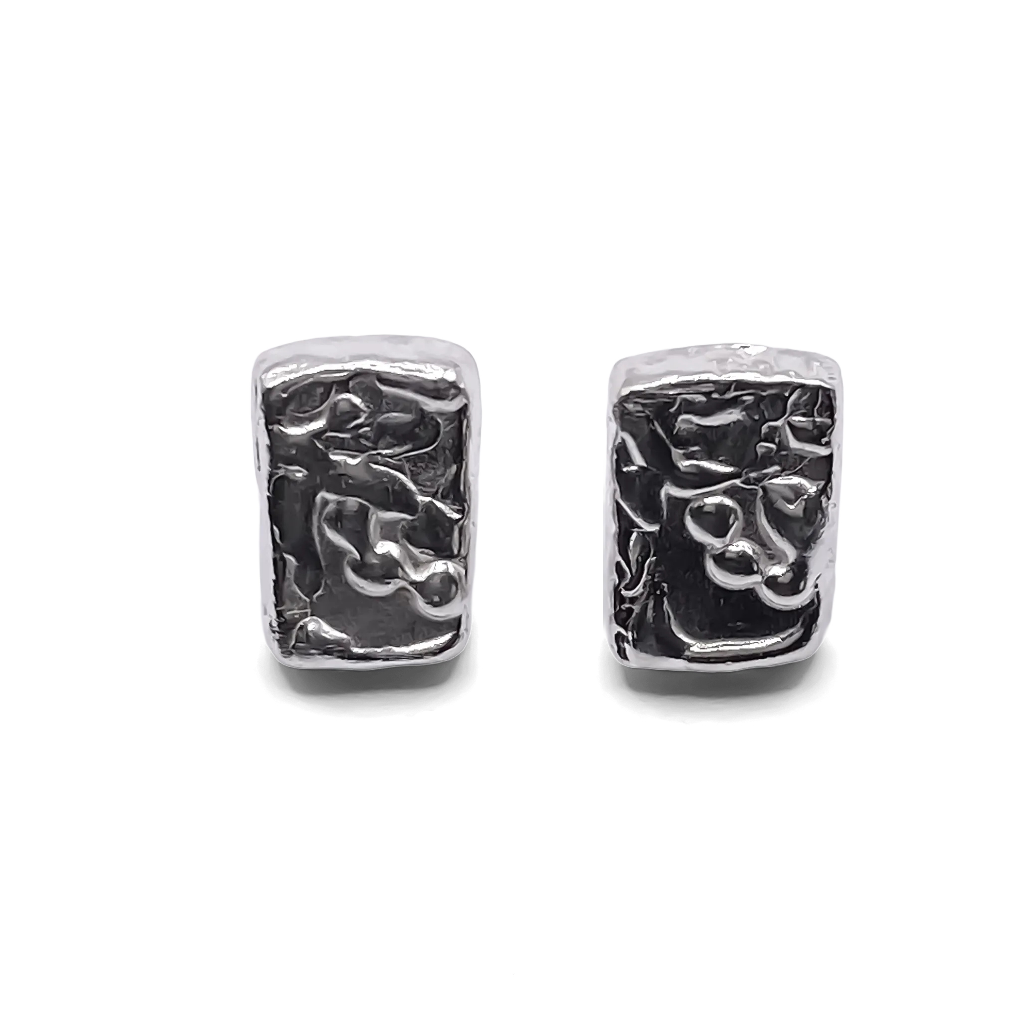Detailed close-up of rectangular sculpted silver earrings with organic texture