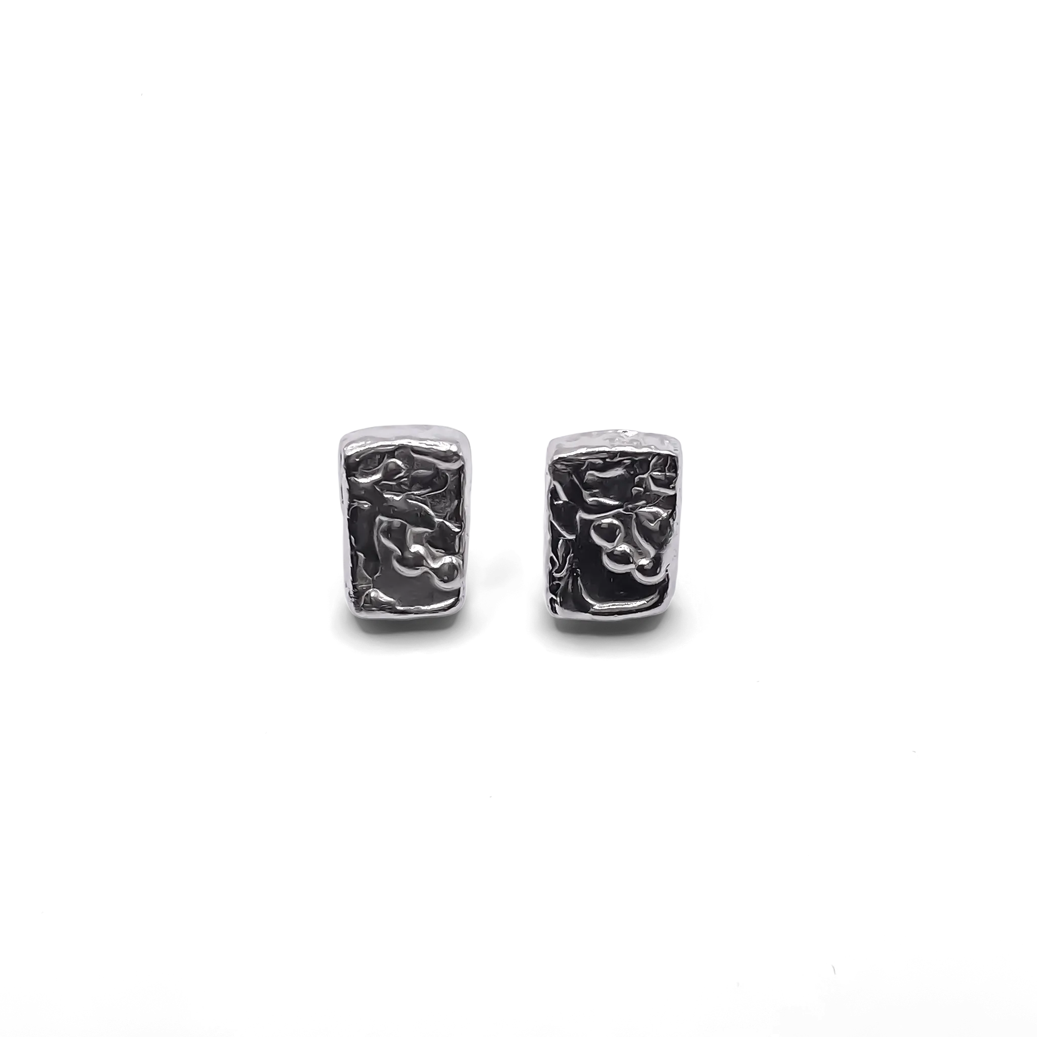 A close-up shot showing the rectangular sculpted earrings worn on the ear. The textured finish catches the light, showcasing the unique detailing and elegant silhouette of each handcrafted piece.