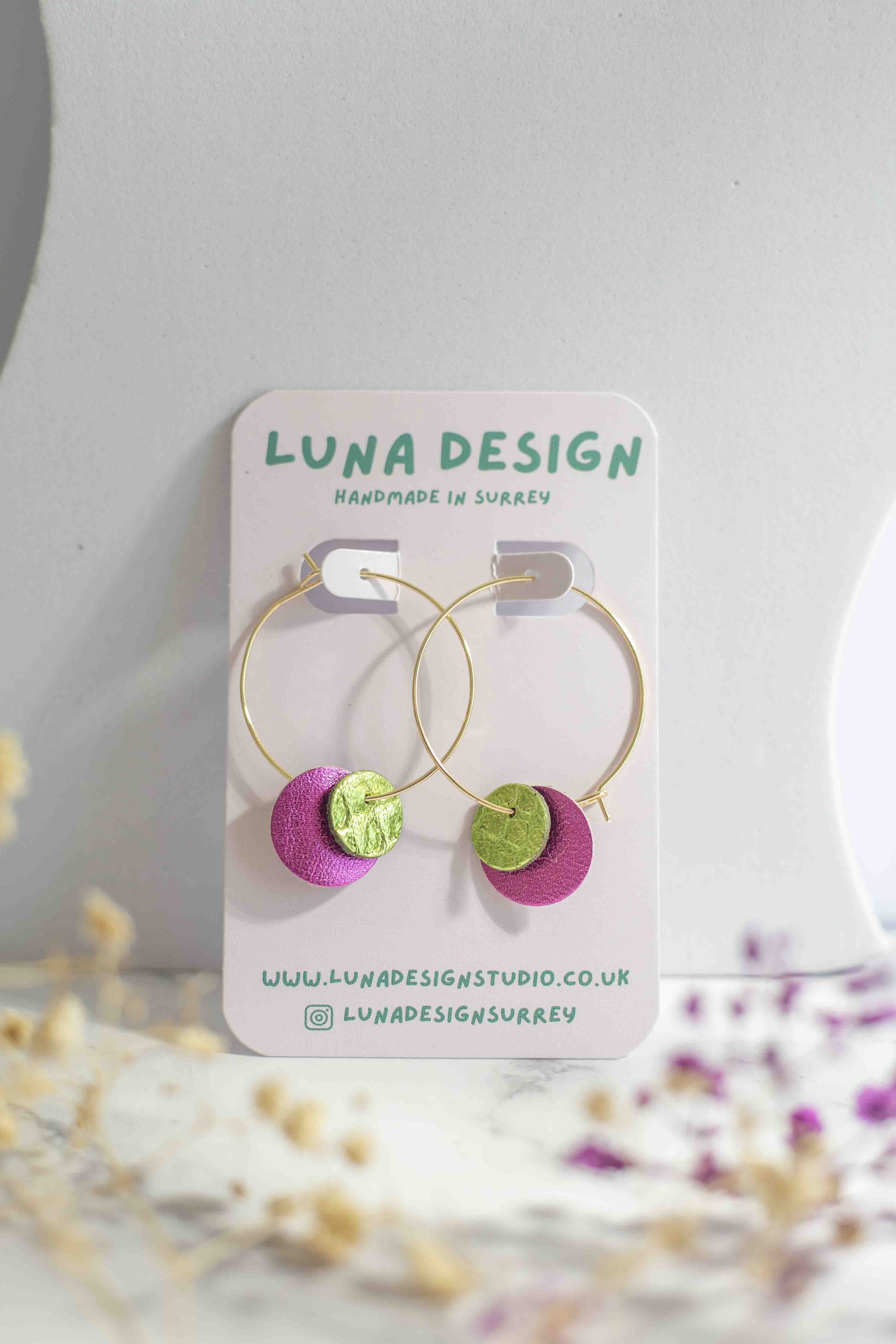 Close-up of pink and green leather circle earrings on 30mm gold-plated hoops, showing texture and stitching detail.