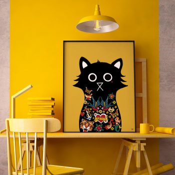 Framed art print of Jerry the tattooed black cat leaning against a bright yellow wall on a wooden desk, surrounded by a yellow lamp, stacked books and a mug