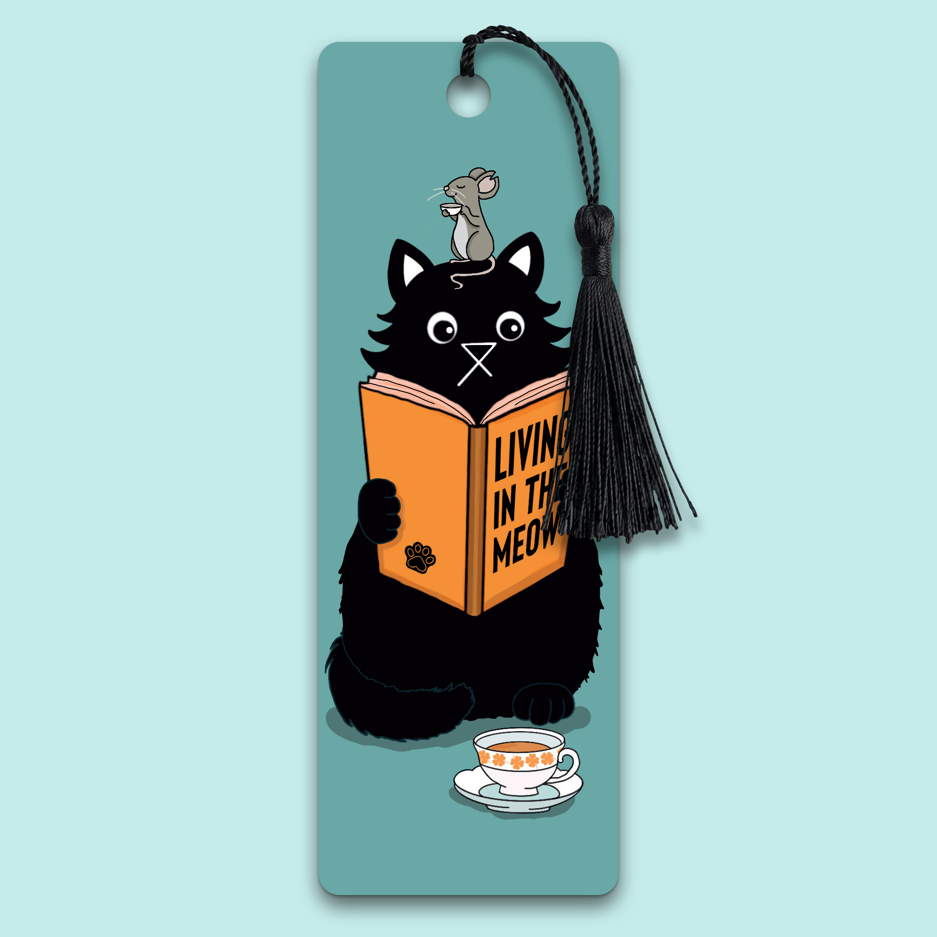 Illustrated bookmark showing a fluffy black cat absorbed in a book titled Living in the Meow, with a tiny mouse perched unnoticed on top of its head. A cup of tea sits on the ground nearby. Teal background. Black tassel attached. Original artwork by Baldy and the Fidget.