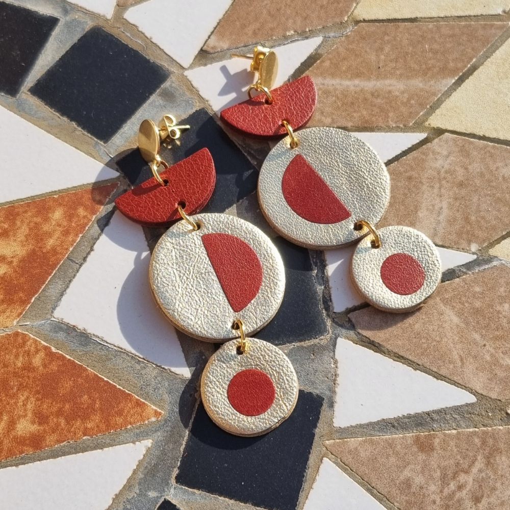 Gold and brick red inlayed dangly earrings on a tiled table.