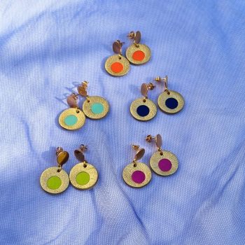 Five pairs of circular leather drop earrings in gold, featuring colourful centre inlays in orange, mint, navy, lime, and magenta, arranged on blue mesh fabric.